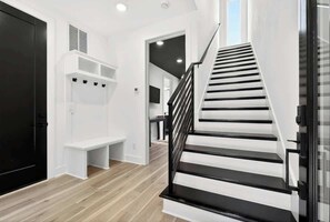 Eine Treppe mit schwarzen Geländern, die zu einer Zwischenebene mit weißen Regalen und einer Bank führt.