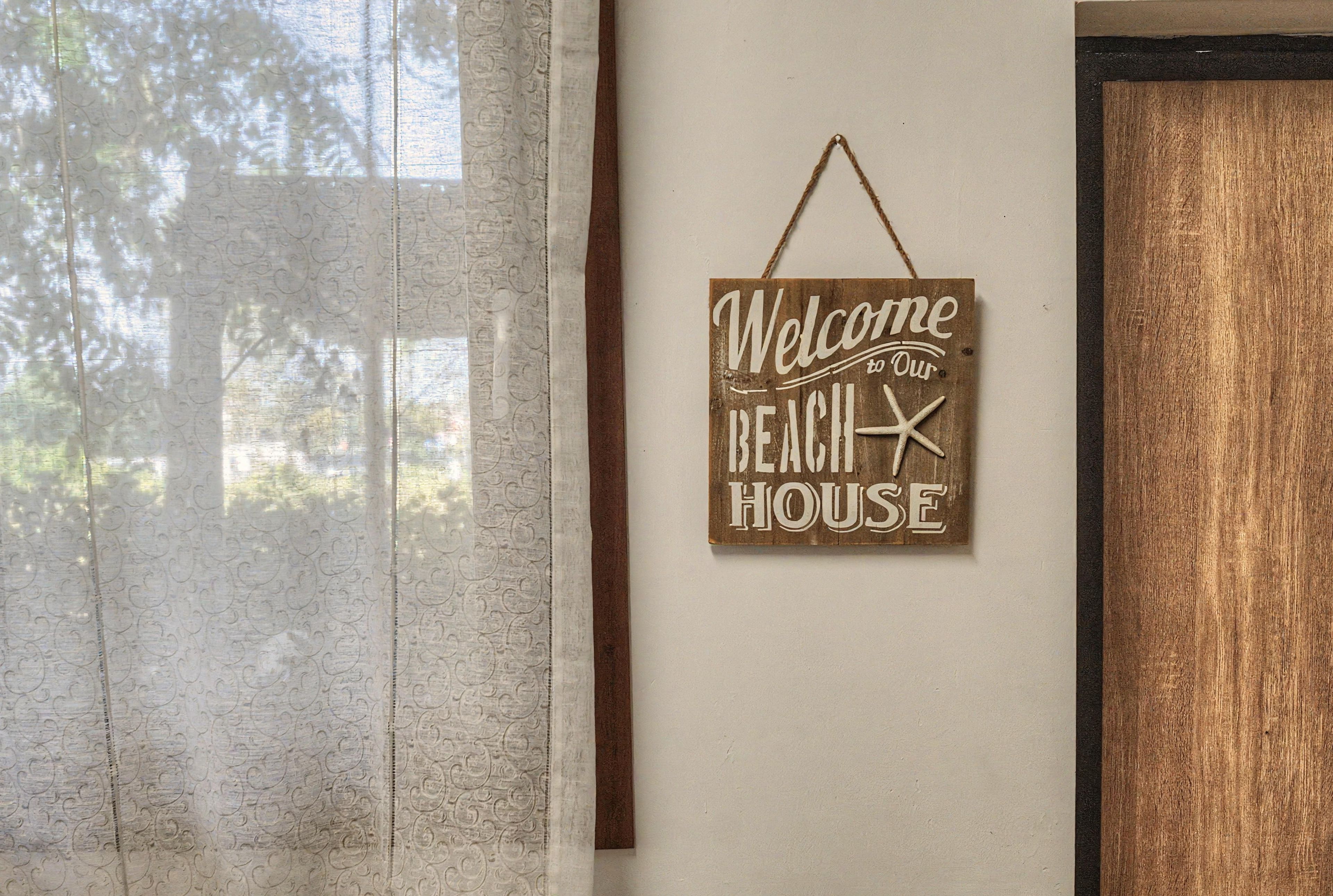 Une enseigne fixée au mur, portant l’inscription « Bienvenue dans notre maison de plage » et ornée d’une étoile de mer.