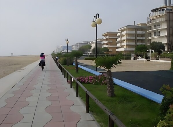 Un paseo marítimo con sendero adoquinado, palmeras y un edificio con balcones.
