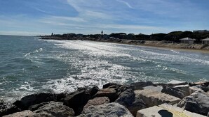 A coastal view with a rocky shoreline, a lighthouse, and buildings along the beach.