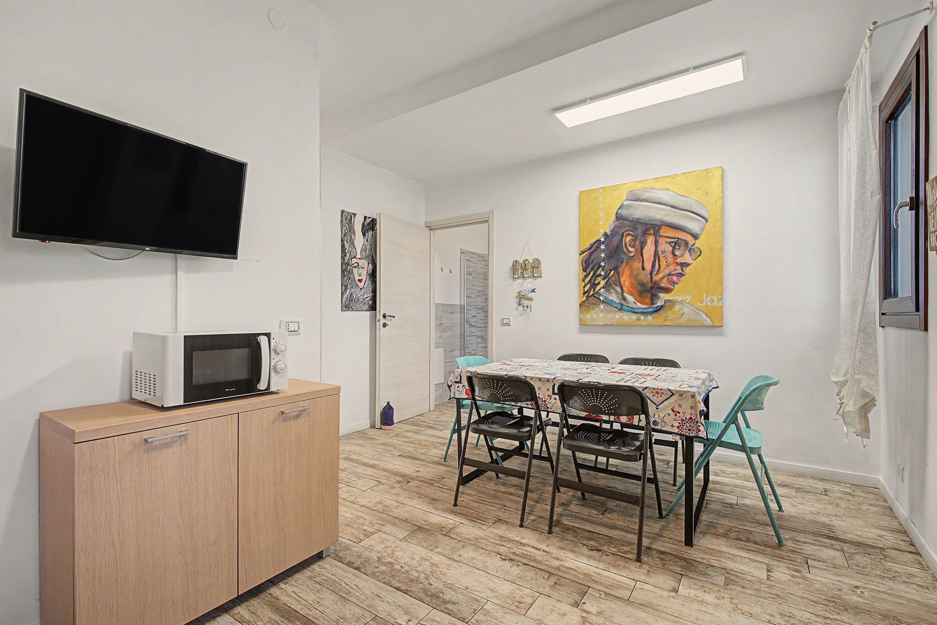 A compact living space with a flat-screen TV, a microwave, a dining table with chairs, and a painting on the wall.