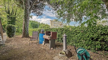 Ein Gartenbereich mit einer Bank, einem blauen Fass, einer Betonkonstruktion und einer Schlauchaufrolle.