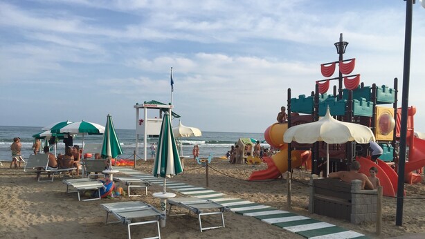 Ein Strand mit Liegestühlen, Sonnenschirmen und einem Spielbereich für Kinder.