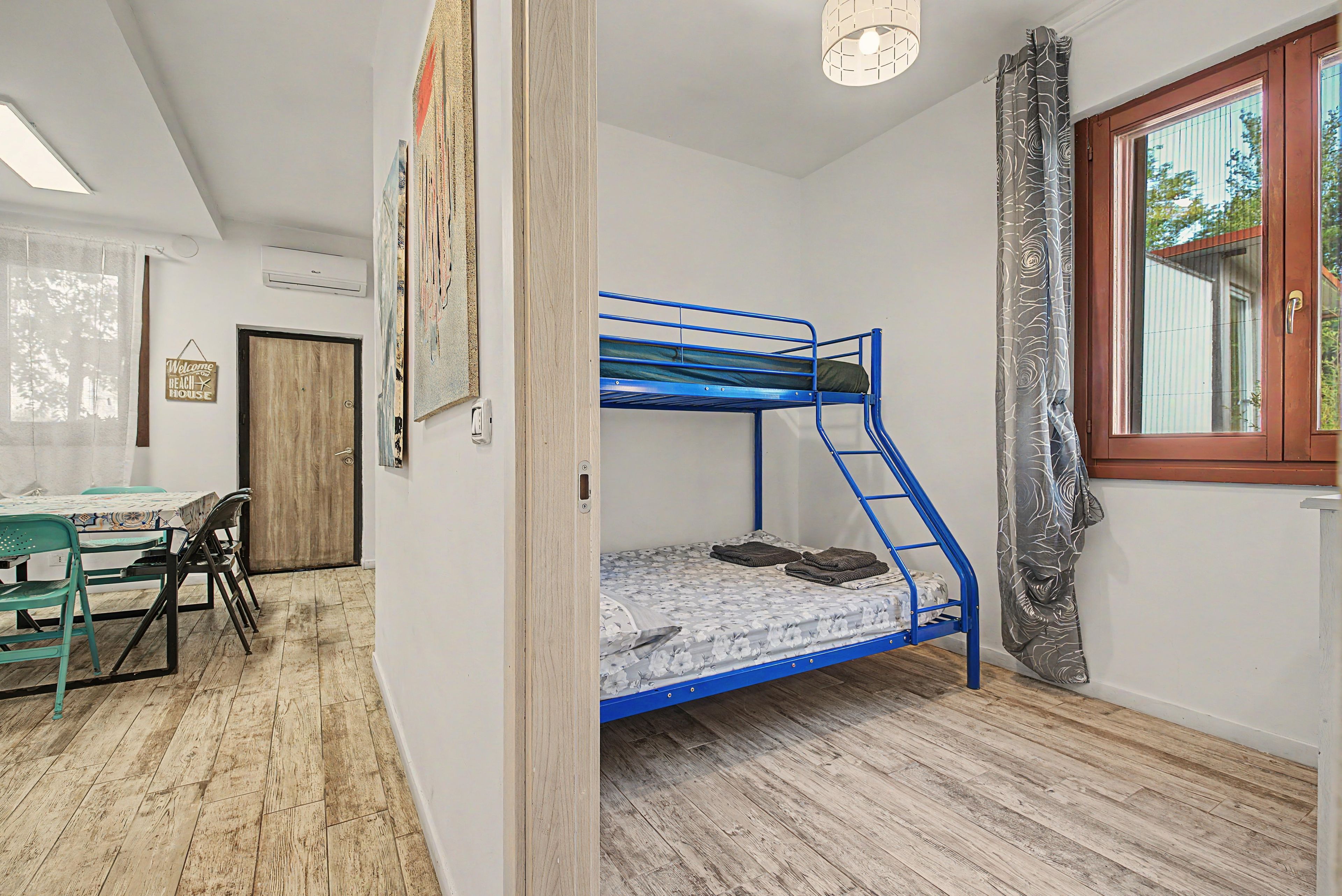 Een kamer met een stapelbed, een bureau, stoelen, een raam met gordijnen en een deur.