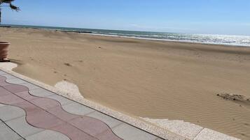 Une plage avec un ciel dégagé, un rivage sablonneux et une promenade dallée.