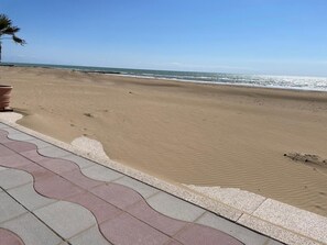 Una playa con cielo despejado, orilla arenosa y un camino empedrado.