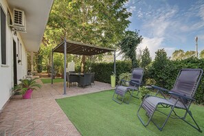 Un patio con una pérgola, muebles de exterior y un pequeño césped.