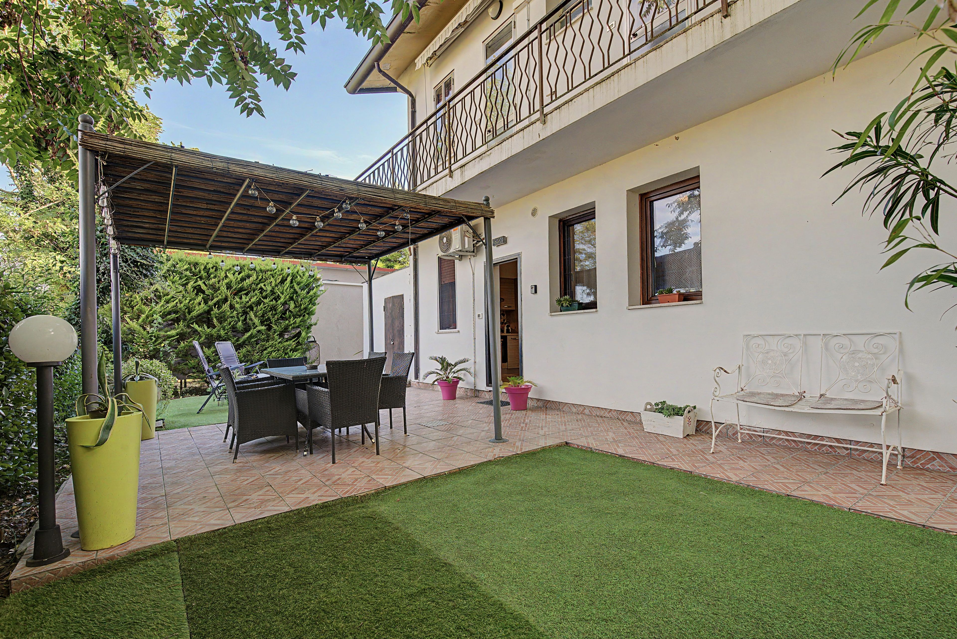 Un'area patio coperta con mobili da esterno, un piccolo prato e piante in vaso.