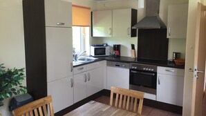Een kleine keuken met witte kastjes, een magnetron, een koffiezetapparaat en een fornuis.