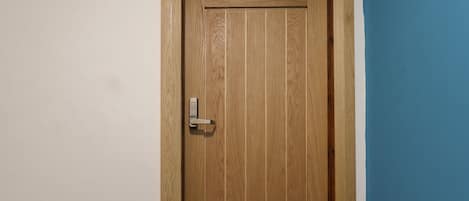 A wooden door with a keypad lock, a small hole at the top, and a white wall adjacent to a blue wall.