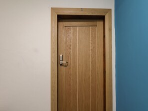 A wooden door with a keypad lock, a small hole at the top, and a white wall adjacent to a blue wall. - Frankies Seaview 3 (Bridlington)