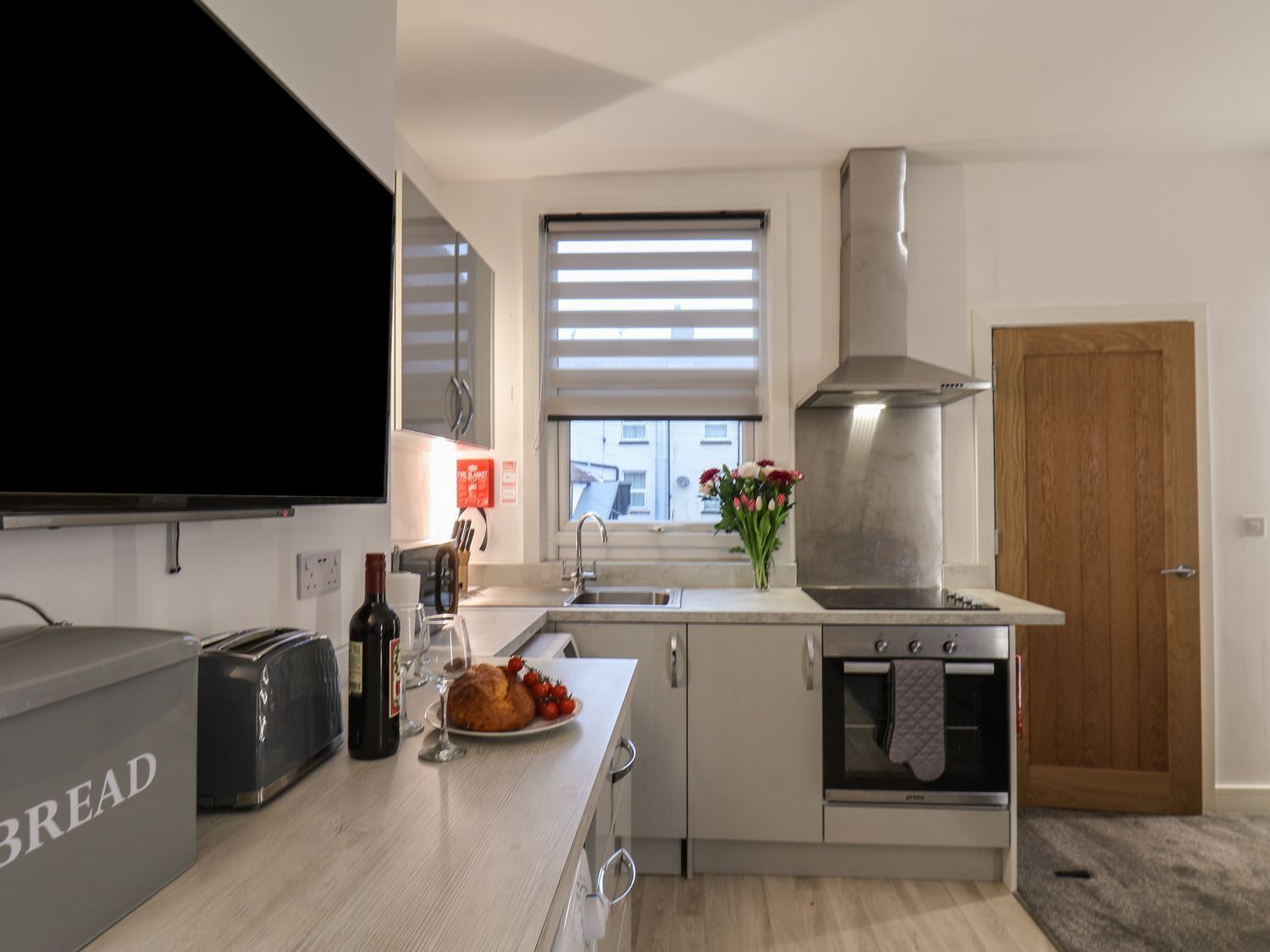 Une cuisine moderne équipée d’un four encastré, d’un évier et d’une grande fenêtre avec des stores.