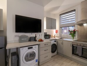 A modern kitchen with a flat-screen TV, built-in microwave, oven, and washing machine. - Frankies Seaview 3 (Bridlington)