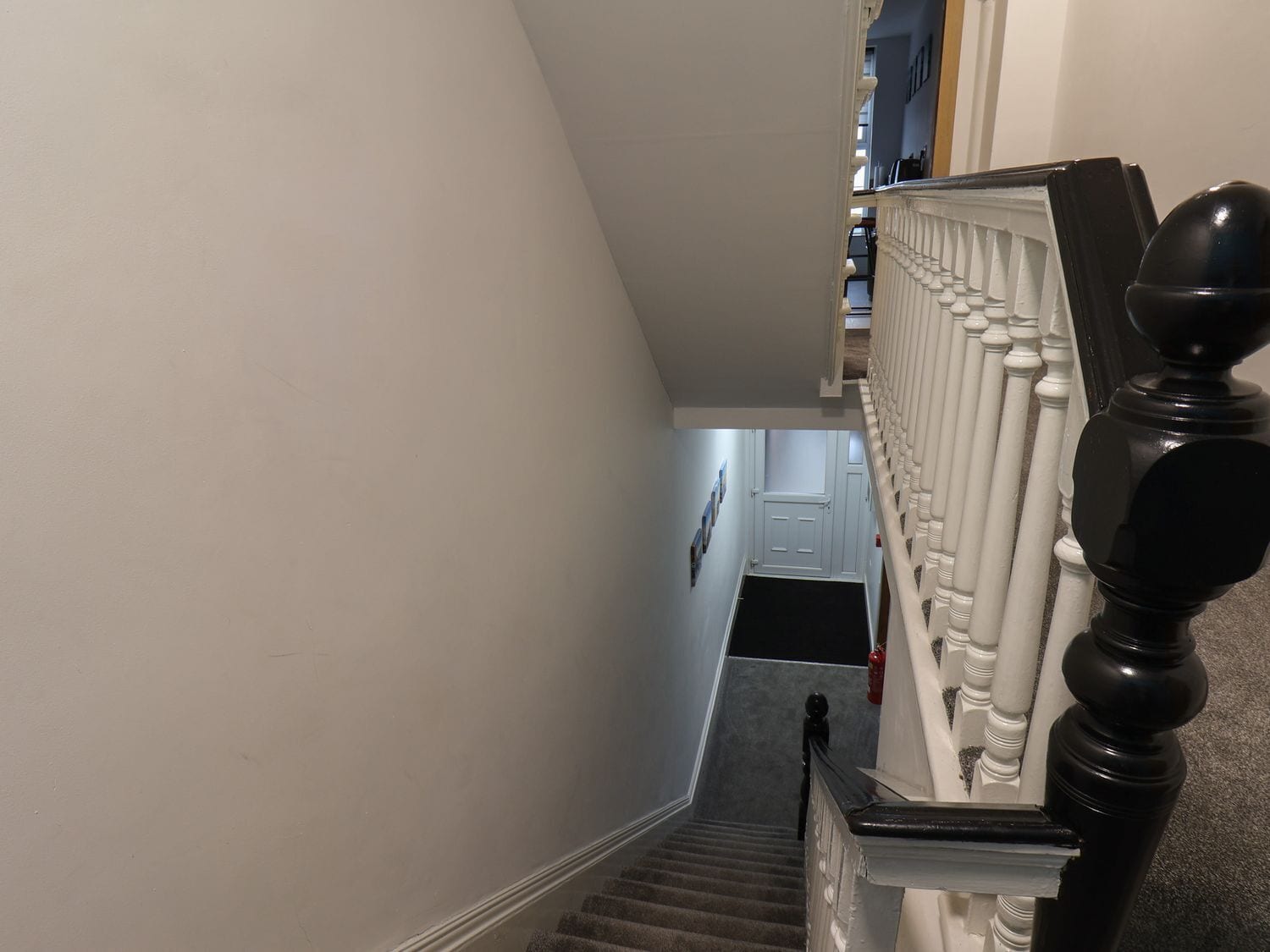 A staircase with white balusters and a black handrail, leading to a landing with a door and a fire extinguisher.