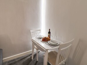 A white dining table with chairs, a loaf of bread, a bottle of wine, and empty glasses. - Frankies Seaview 3 (Bridlington)