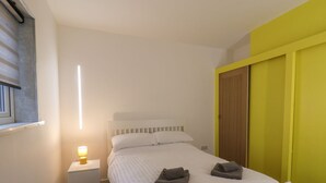 Ein Schlafzimmer mit Bett, Nachttisch, Lampe und einer gelben Wand.