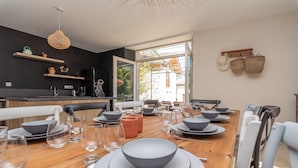 Un coin repas avec une table en bois dressée pour le repas, une cuisine équipée d’appareils modernes et une vue sur l’extérieur, visible à travers une porte vitrée.