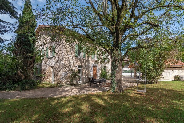 Un edificio de piedra con encanto rústico, una puerta de madera y un columpio en el patio.