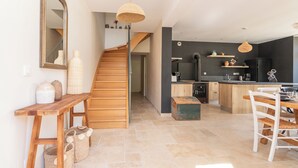 Une cuisine moderne avec un escalier en bois, un coin repas avec une table et des chaises blanches, et un grand miroir au mur.