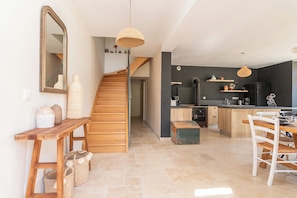 Une cuisine moderne avec un escalier en bois, un coin repas avec une table et des chaises blanches, et un grand miroir au mur.