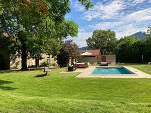 Un patio trasero con piscina, un edificio de piedra y un árbol grande.