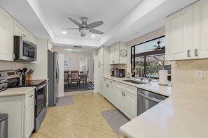 Una cocina moderna con electrodomésticos de acero inoxidable, armarios blancos y un amplio ventanal.