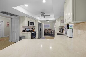 A modern kitchen with a central island, built-in appliances, and a dining area with chairs and a table. - Pink Flamingo Pool House-Luxury Tropical Escape (Cape Coral)