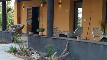 Un'area salotto esterna riparata, con sedie e tavoli, piante in vaso e un muro in pietra.
