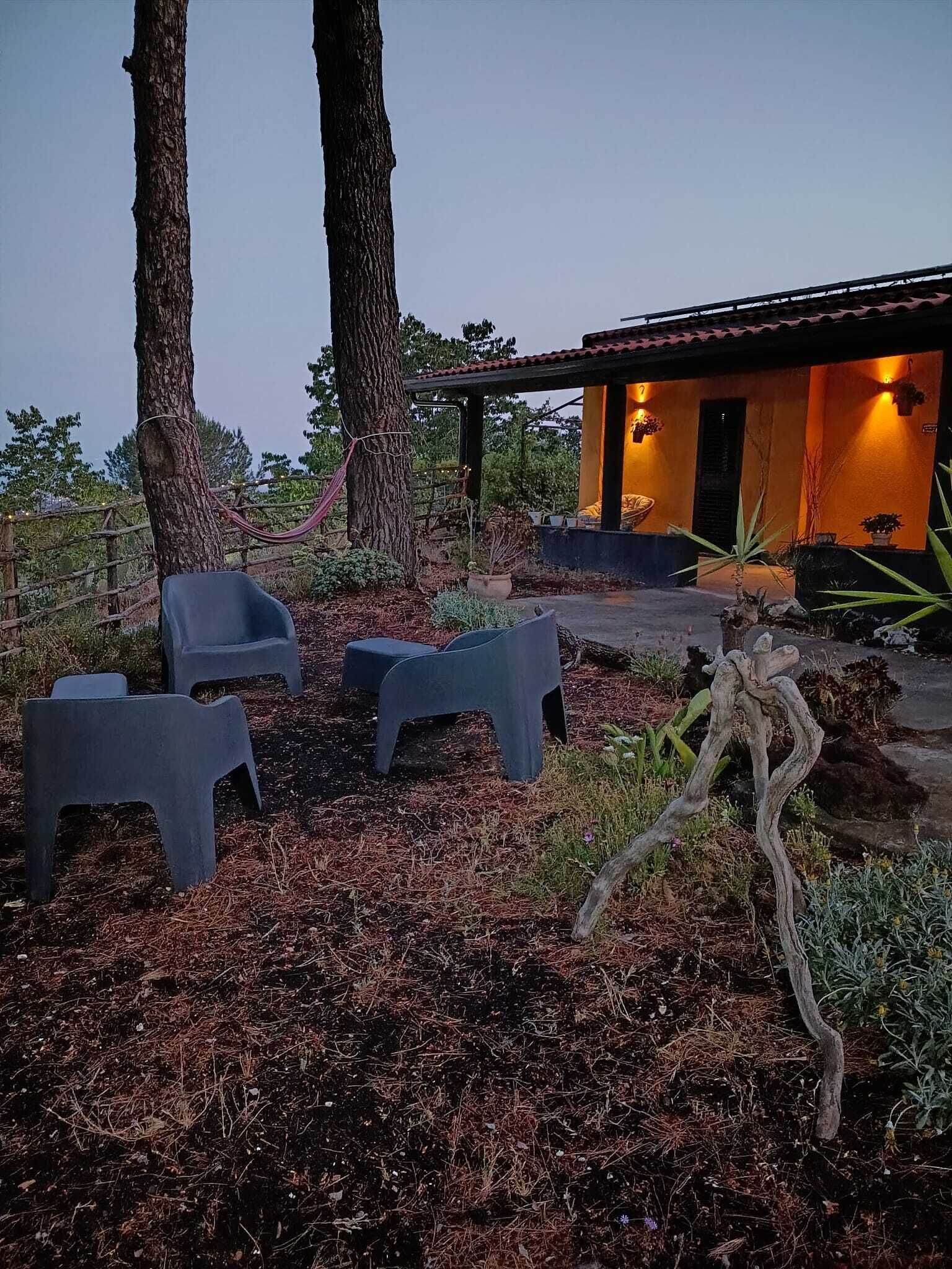 A modern outdoor seating area with plastic chairs, a hammock, and a rustic wooden sculpture.