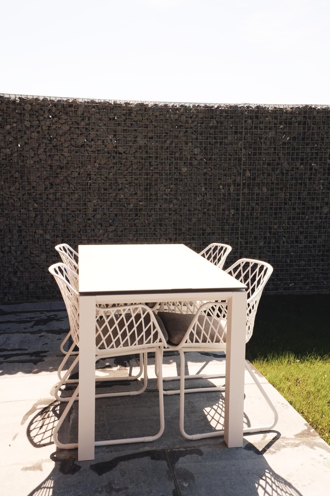 A white metal table with four chairs, set against a stone wall.
