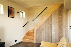 Una escalera con escalones de madera y barandillas negras, un cuadro de un caballo en la pared y una puerta a la derecha.