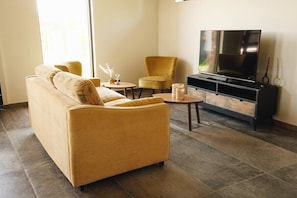 Een moderne woonkamer met een bank, fauteuil, salontafel en een flatscreen televisie.