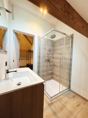 Un baño moderno con cabina de ducha de vidrio, un lavabo blanco y suelo de madera.