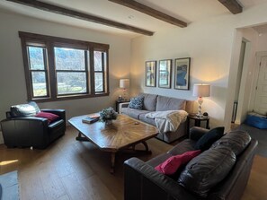 Una sala de estar con sofá, mesa de centro, chimenea y ventana con vista a árboles.