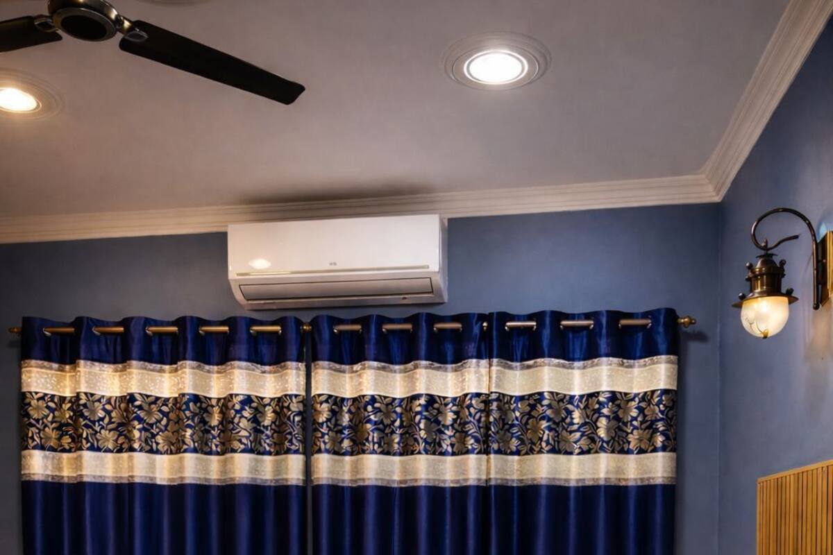 A hotel room with a bed, a ceiling fan, an air conditioning unit, and a window with curtains.