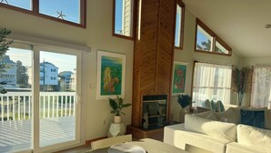 A spacious living room with a large sliding glass door leading to a balcony, a fireplace, and a cozy seating area. - The Odyssey - Waterfront with Dock + Boat Lift + NH Village Beach Club Member! (Kill Devil Hills)