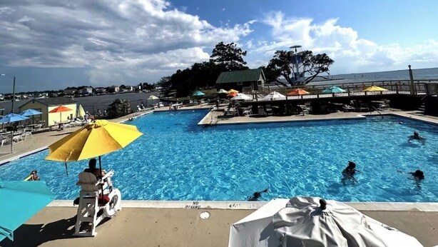 A swimming pool with multiple lanes, umbrellas, and lounge chairs. - The Odyssey - Waterfront with Dock + Boat Lift + NH Village Beach Club Member! (Kill Devil Hills)