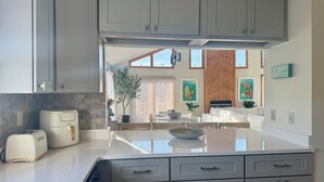 A modern kitchen with grey cabinets, a built-in oven, and a dining area with a white sofa and a table. - The Odyssey - Waterfront with Dock + Boat Lift + NH Village Beach Club Member! (Kill Devil Hills)