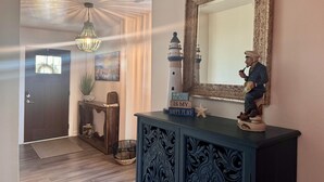A hallway with a wooden door, a decorative mirror, a lighthouse figurine, and a sign that reads 'The Beach is My Happy Place.' - The Odyssey - Waterfront with Dock + Boat Lift + NH Village Beach Club Member! (Kill Devil Hills)
