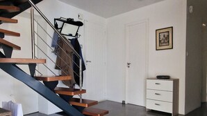 Una escalera con barandilla metálica, una pared blanca con un cuadro enmarcado y un mueble blanco pequeño.