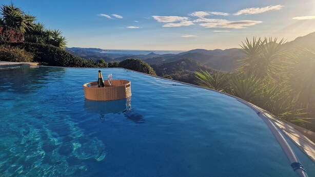 Una piscina infinita de color azul claro con una cesta de mimbre que contiene una botella y un vaso.
