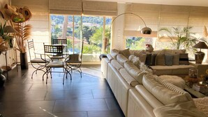 A spacious living area with a sofa, a dining table with chairs, and a view of greenery outside. - Villa for 7 guests with private pool and hot tub near Cannes (Fréjus)