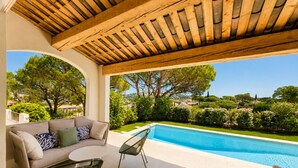 Un espace extérieur abrité comprenant une piscine, un canapé et des fauteuils.