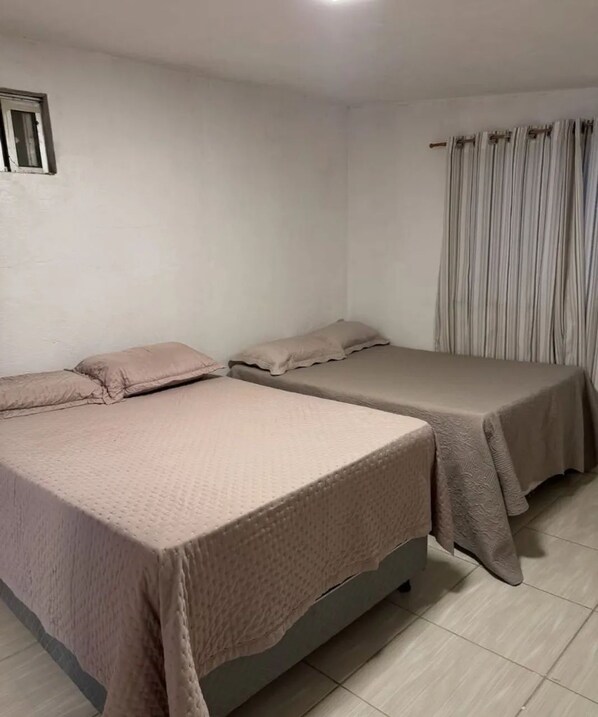 A room with two beds, a window with curtains, and a tiled floor.
