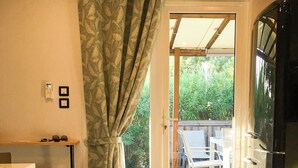 A room with a sliding glass door leading to an outdoor deck, a white table, and a refrigerator. - Mobil home for 6 guests – Gulf of Saint-Tropez 4★ (La Garde-Freinet)