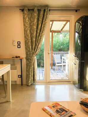 A room with a sliding glass door leading to an outdoor deck, a white table, and a refrigerator. - Mobil home for 6 guests – Gulf of Saint-Tropez 4★ (La Garde-Freinet)