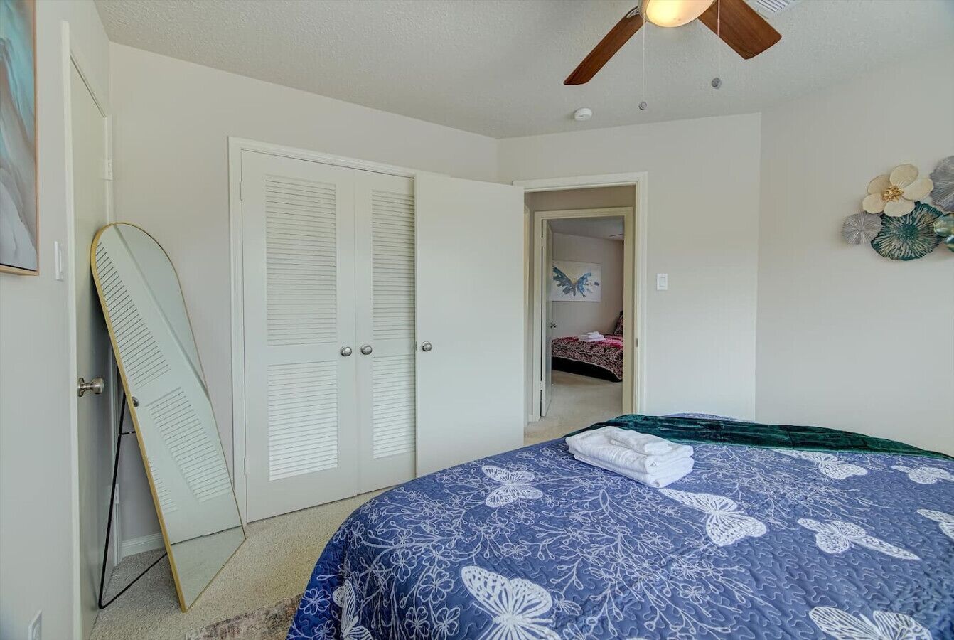 A bedroom with a bed, a ceiling fan, a door, and a mirror.