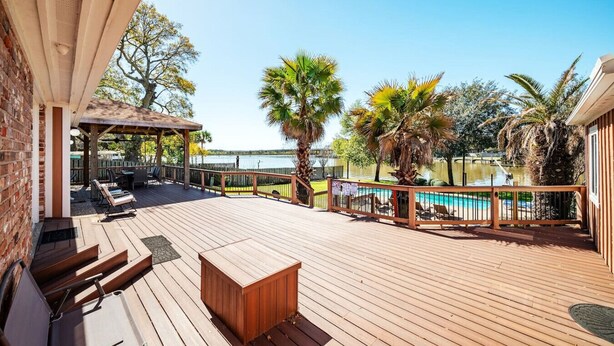 Una terraza de madera con piscina, sillas de descanso y un área de estar cubierta.