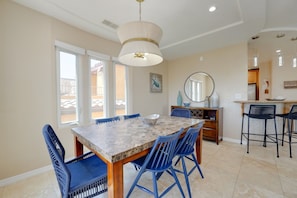A dining area with a marble table, blue chairs, a chandelier, and a view through large windows. - South Mission Sand & Surf Retreat with AC & 3 Car Garage! (San Diego)