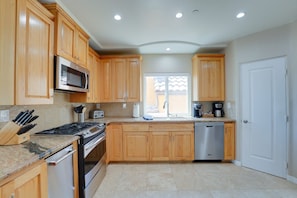 A kitchen with wooden cabinets, a microwave, a stove, a dishwasher, and a window with a view. - South Mission Sand & Surf Retreat with AC & 3 Car Garage! (San Diego)